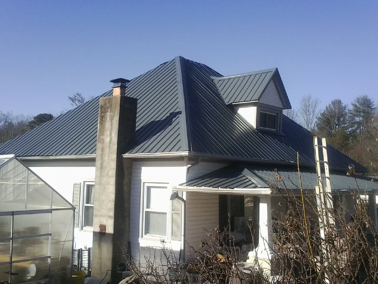 Dark blue standing seam metal roof on a white farmhouse with dormer — Slate & Tile Roof Repair by Roofing Brothers in Nunda
