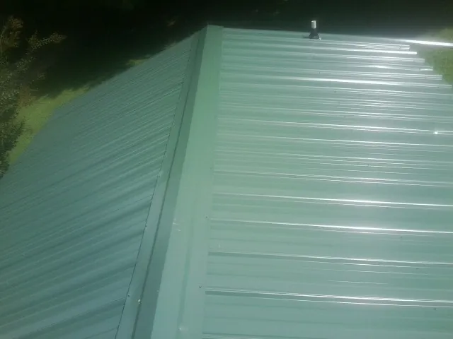 New green metal panels meeting at the ridge of a roof — Flat Roof Repair work by our crew in Nunda