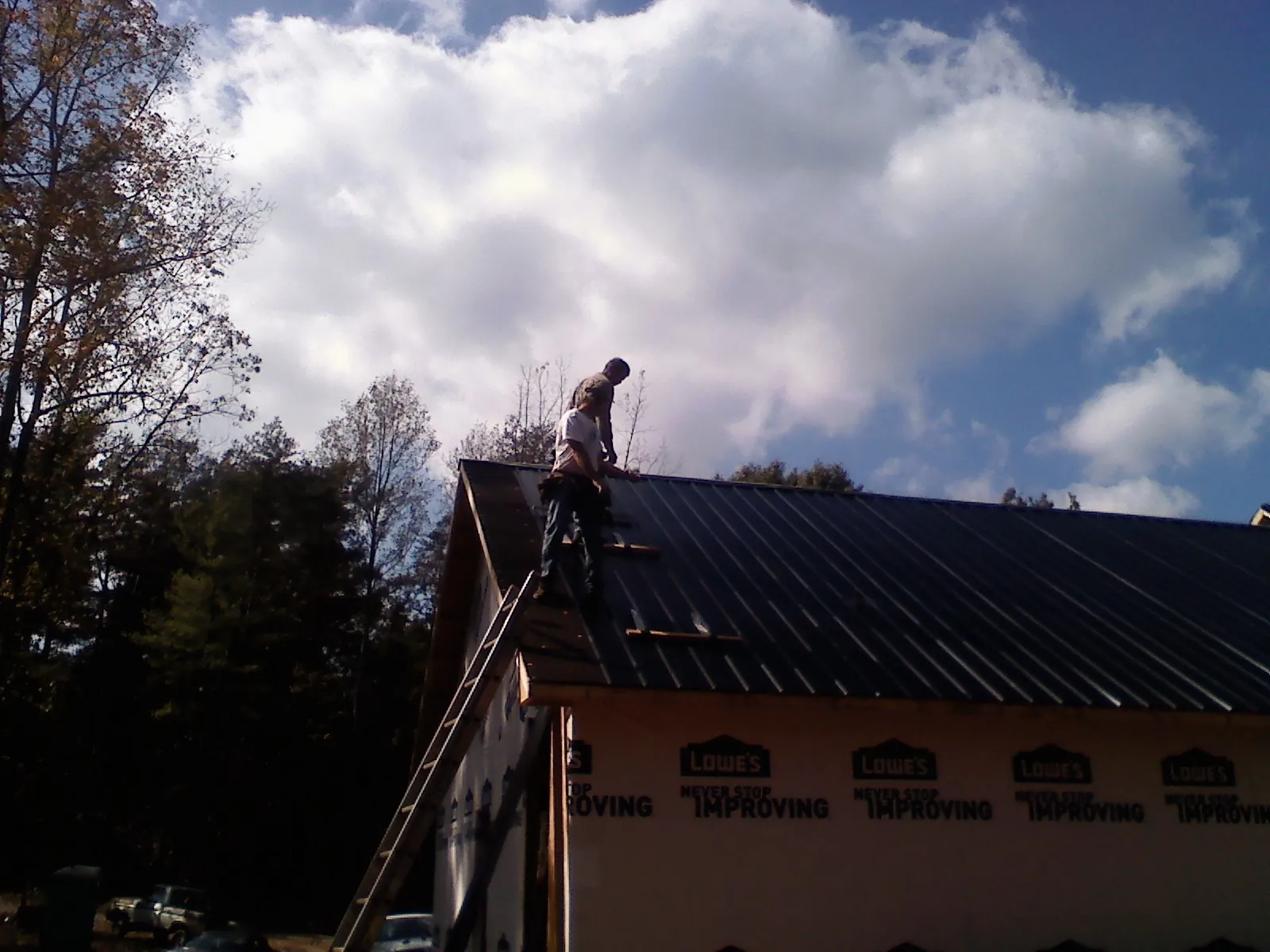 Roofer fastening dark metal panels high against a cloudy sky, from a Roof Inspection job in Nunda