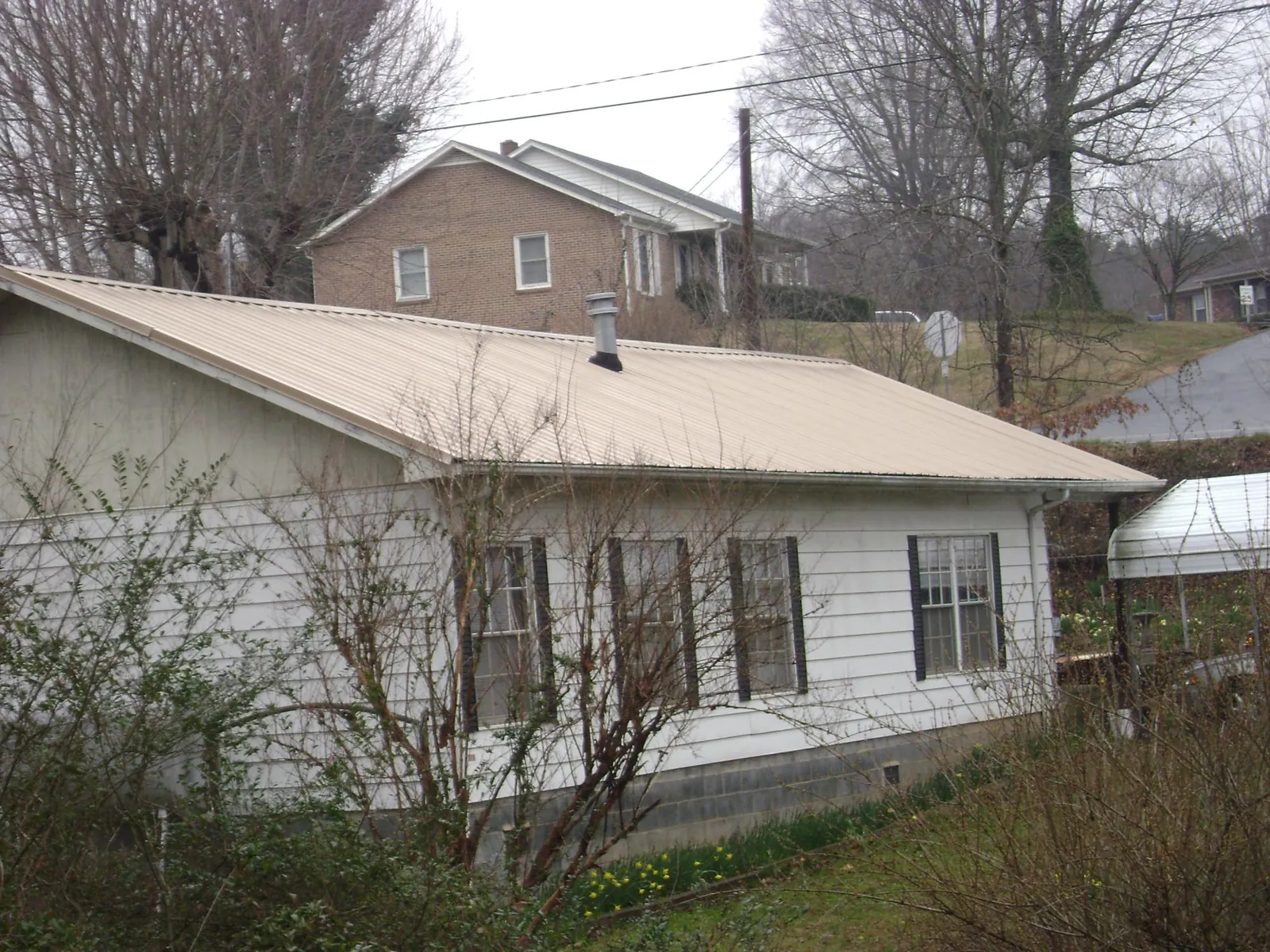 Tan metal roof on a white sided house set into a hillside — Commercial Roofing by Roofing Brothers in Nunda