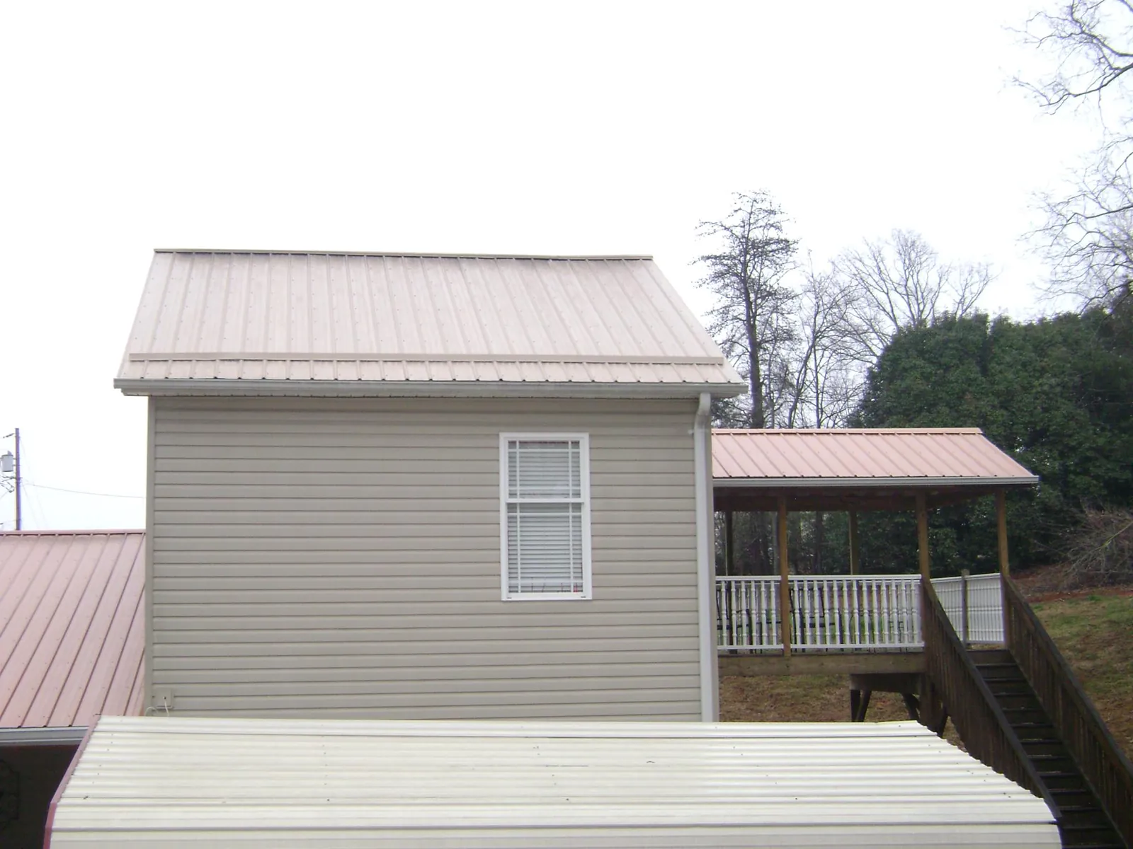 Tan metal roofs on a two story addition and attached porch, from a Roof Replacement job in Nunda